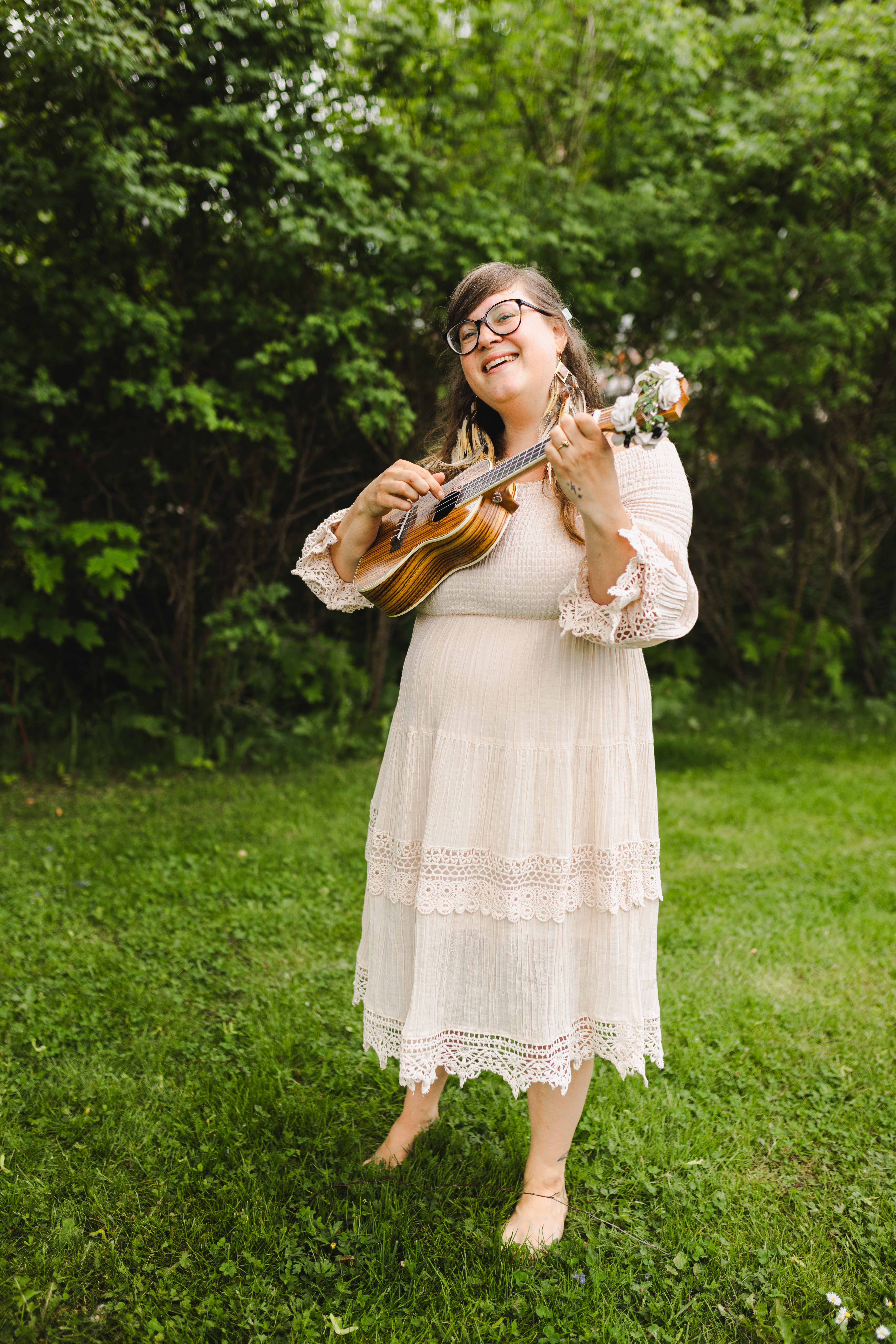 Emma D Haglund spelar ukulele framför en grön bakgrund av träd och gräs